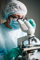 Wall Mural - scientist in blue medical gloves and uniform learning samples with microscope in laboratory.