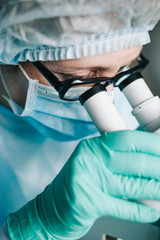 Wall Mural - scientist in blue medical gloves and uniform learning samples with microscope in laboratory.