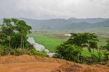 Wall Mural - River and dirt road with mountains and lush vegetation at Ring Road in Cameroon, Africa