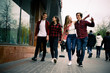 © dashamuller - Four happy trendy teenage friends walking in the city, talking each other and smiling. Lifestyle, friendship and urban life concepts.
