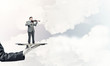 © adam121 - Businessman on metal tray playing violin against blue sky background