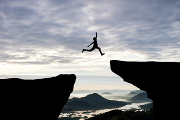 man jump through the gap between hill.man jumping over cliff on sunset background,business concept i