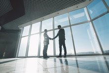Two Young Businessmen Are Shaking Hands With Each Other Standing Against Panoramic Windows.