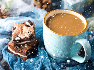 Cream cheese brownies with cookies on blue and mug of coffee and milk. Winter Holiday background with baubles and falling snow