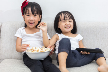 Wall Mural - Happy Asian Chinese little sisters eating popcorn on the sofa