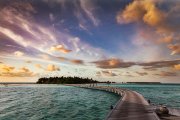 Wall Mural - Wooden jetty towards a small island in Maldives at sunset