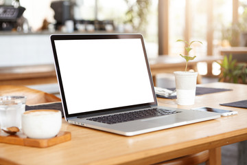 Close up minimalist shot of generic laptop computer and working accessories resting on wooden table against blurred background of cafeteria. Workplace of unknown freelancer. Selective focus