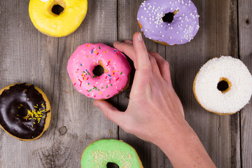 Hand taking pink donut on wooden background