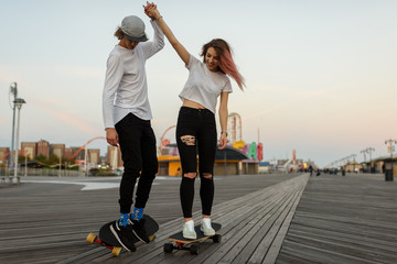 Young couple learning how to ride a longboard, holding hands