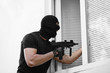 © Africa Studio - Thief with gun entering house through window