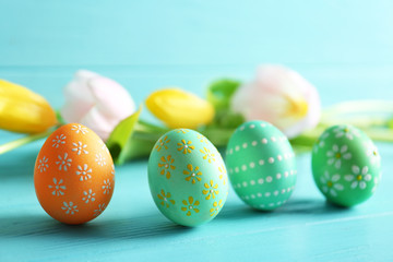 Wall Mural - Beautiful Easter eggs and flowers on blue wooden background, closeup