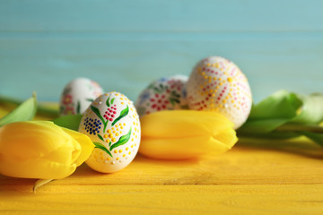 Wall Mural - Beautiful Easter eggs and flowers on yellow wooden table, closeup