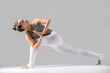 © fizkes - Young attractive woman practicing yoga, standing in Revolved Side Angle exercise, Parivrtta Parsvakonasana pose, namaste, working out wearing sportswear, indoor full length, grey studio background