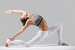 Young attractive woman practicing yoga, standing in Horse rider exercise, anjaneyasana pose, working out wearing sportswear, white pants, gray top, indoor full length, grey studio background