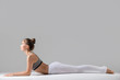© fizkes - Young attractive woman practicing yoga, sitting in Sphinx, Cobra, exercise, Ardha bhudjangasana pose, working out wearing sportswear, indoor full length, isolated against grey studio background
