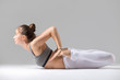 Young attractive woman practicing yoga, stretching in Frog exercise, Bhekasana pose, working out wearing sportswear, white pants, bra, indoor full length, isolated against grey studio background