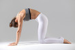 © fizkes - Young attractive woman practicing yoga, standing in asana paired with Cow Pose on the inhale, Cat exercise, Marjaryasana pose, working out in sportswear, indoor full length, grey studio background