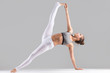 © fizkes - Young attractive woman practicing yoga, stretching in Side Plank exercise, Full Version of Vasisthasana pose, working out wearing sportswear, indoor full length, isolated, grey studio background