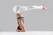 © fizkes - Young attractive woman practicing yoga, standing in headstand exercise, variation of salamba sirsasana pose, working out wearing sportswear, indoor full length, isolated, grey studio background