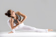 © fizkes - Young woman practicing yoga, stretching in Revolved Head to Knee Forward Bend exercise, Baddha Ardha Samakonasan pose, working out wearing sportswear, indoor full length, grey studio background