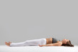 Young attractive woman practicing yoga, lying in Dead Body, Corpse exercise, Savasana pose, working out wearing sportswear, indoor full length, isolated against grey studio background