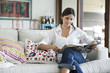 © PhotoAlto - Woman reading magazine while sitting on sofa at home