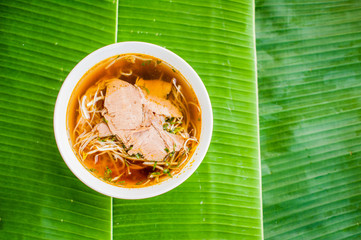 A bowl of Traditional Vietnamese beef soup Pho Bo on banana leaf background.