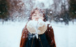 © estradaanton - Winter. Woman with red hair wearing ear muffs blowing on snow in hands