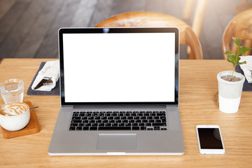 Technology, business and communication concept. Front view of minimalist workspace of freelancer: modern laptop computer with copy space for your design resting on table with mobile phone and drinks