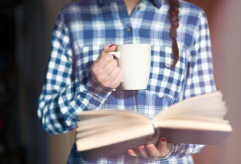 Close up of woman hands holding a book and a cup of coffee Red nails winter nail art and student home education concept