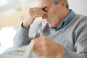 Senior man having a headache reading newspaper