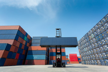 Forklift truck lifting cargo container in shipping yard or dock yard against blue sky with cargo container stack in background for transportation import,export and logistic industrial concept