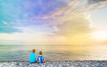 Two Small Kids Sitting On The Beach And Enjoying  Beautiful Sunset.