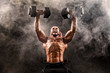 Bald Topless Muscular Man Doing Exercises With Two Dumbbells On Bench Press In Smoke