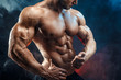 © ZaStock - Unrecognizable Strong bald bodybuilder with six pack. Bodybuilder man with perfect abs, shoulders,biceps, triceps and chest, personal fitness trainer flexing his muscles in blue, red smoke