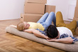 © Drpixel - Young couple laying on carpet and discussing house project with boxes in the background.