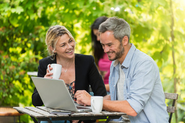 Wall Mural - A smart couple is sitting at a terrace cafe and using a laptop