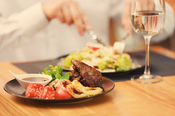 Plate with tasty meat, fried vegetables and sauce on table in restaurant with client on background