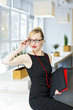 © wimages - Attractive blonde girl corrects her glasses as she sits on a table in front a window in an office