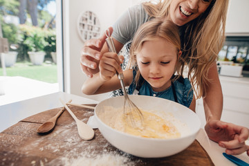 Wall Mural - Young girl with her mother mixing batter at home