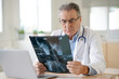 © goodluz - Portrait of senior doctor examining X-ray