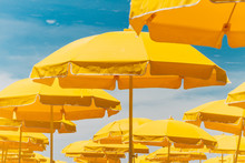 Several Yellow Umbrellas On The Beach Against Blue Sky With Clou