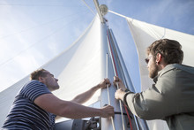 Two Men Hoisting Sail On Yacht