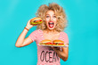 Studio fashion portrait of a beautiful funny young girl on the turquoise background, blonde holding a tray burger is going to bite a hamburger, curly hair, perfect makeup, crazy emotions, fast food