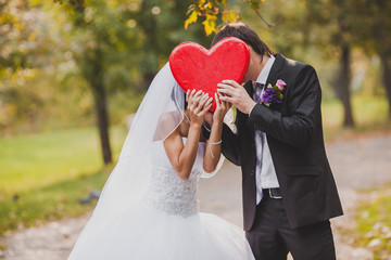 Happy wedding couple holds big red heart in hands.