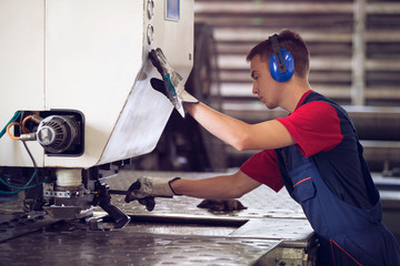 Wall Mural - Inside a factory, industrial worker in action on metal press machine holding a steel piece ready to be worked. 
