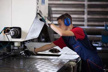 Inside a factory, industrial worker in action on metal press machine holding a steel piece ready to be worked. 
