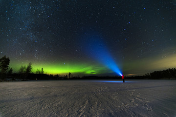 person puts bright blue flashlight to the starry sky with green north lights using torch staying on frozen lake 