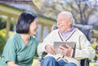 © jovannig - Happy elder patient in rehab clinic garden using tablet and smil