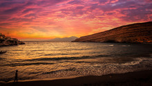 Stunning Sunset At Matala Beach On Crete Island, Greece. There Is A Girl Walking On The Beach. The Colors In The Sky Are Very Beautiful, Yellow, Orange And Red.